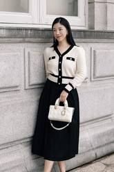a lady in a white cardigan with black trim and a black skirt